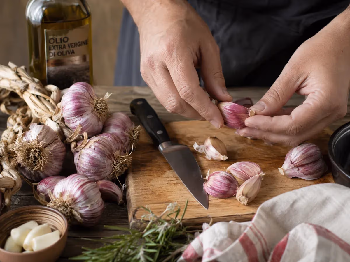 Mani di cuoco separano spicchi di aglio rosso viola su tagliere in legno con coltello