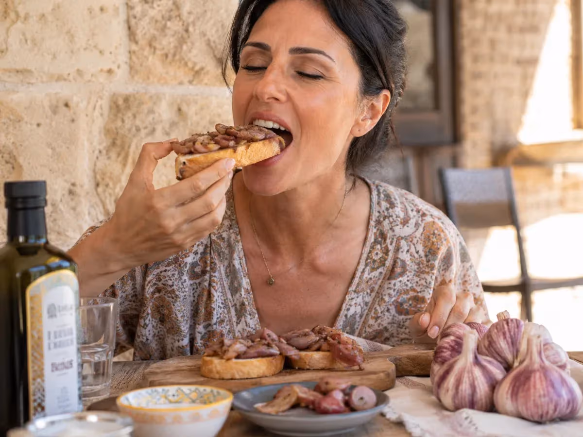 Donna assaggia bruschetta con aglio rosso caramellato accanto a tavola con olio extravergine
