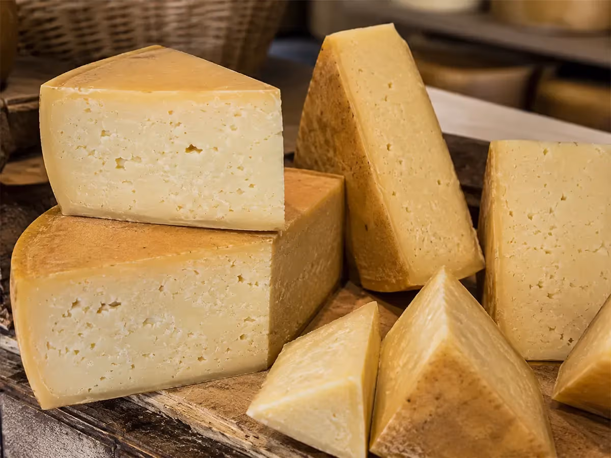 Più pezzi triangolari di Asiago DOP con crosta dorata impilati su superficie in legno rustico