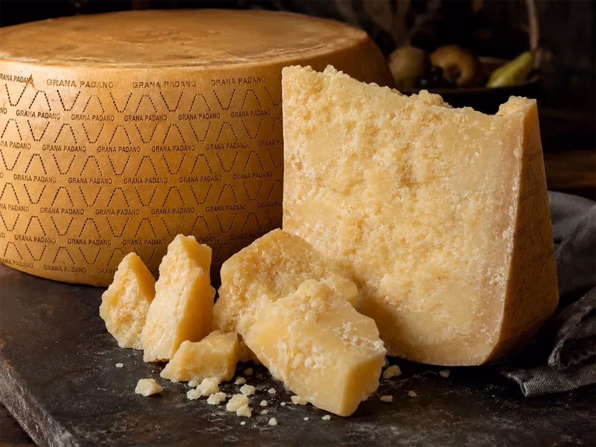 Forma intera di Grana Padano con spicchio e briciole su superficie scura