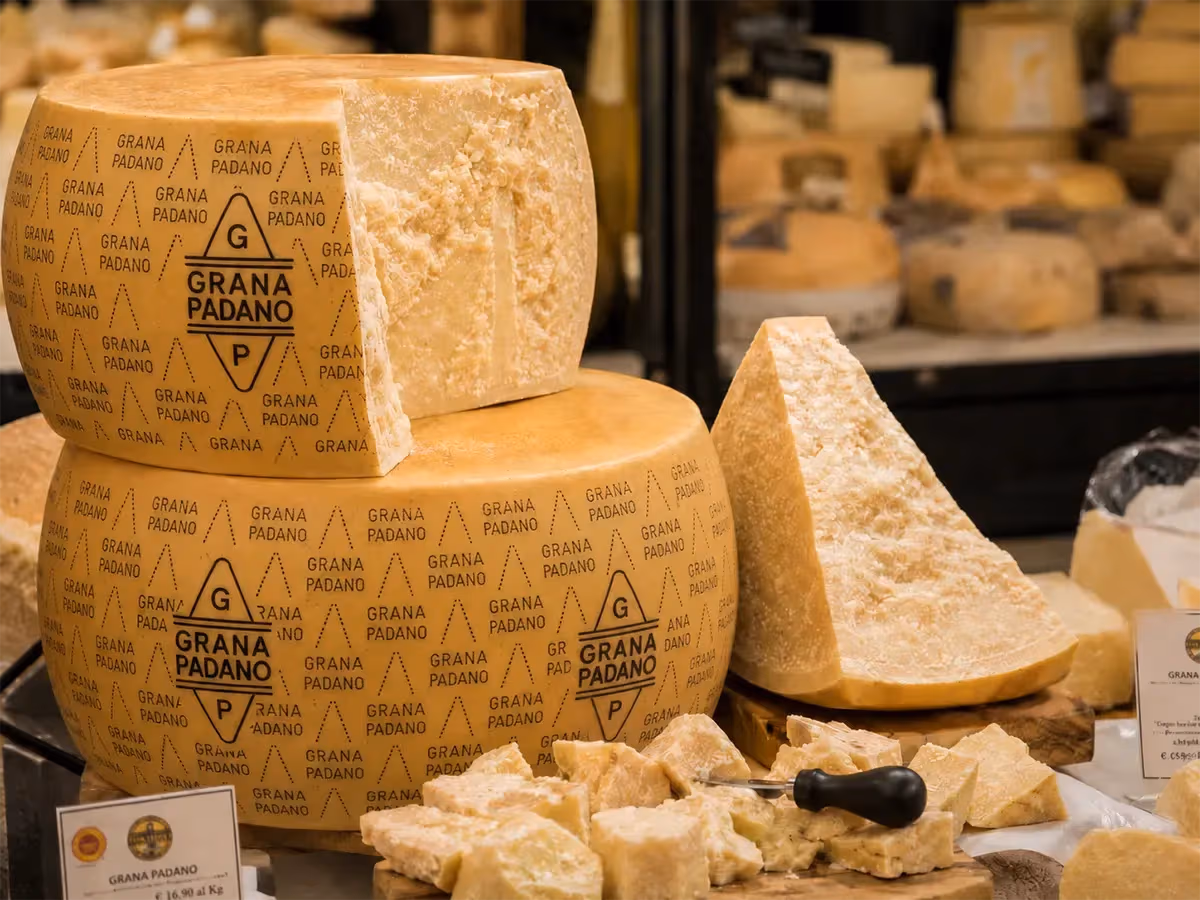 Due forme intere di Grana Padano sovrapposte con spicchi in esposizione al mercato