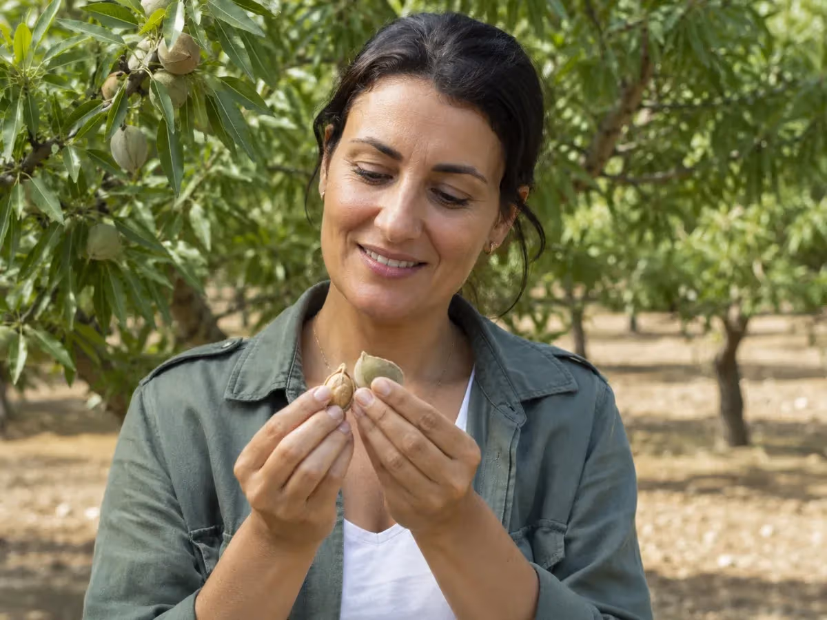 Donna sorridente in mandorleto tiene tra le mani una mandorla appena aperta con guscio verde