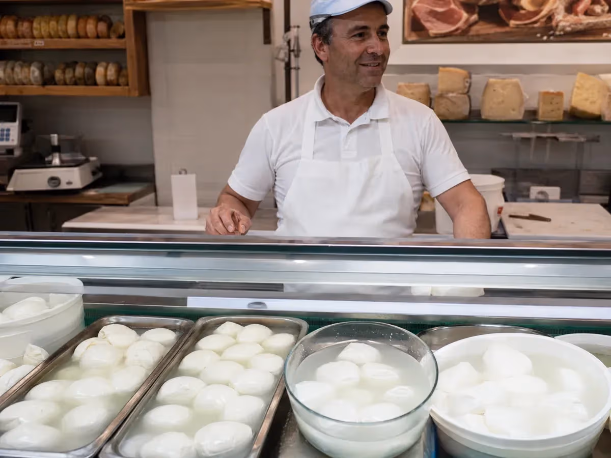 Venditore sorridente dietro bancone con vassoi colmi di mozzarelle fresche in latteria italiana