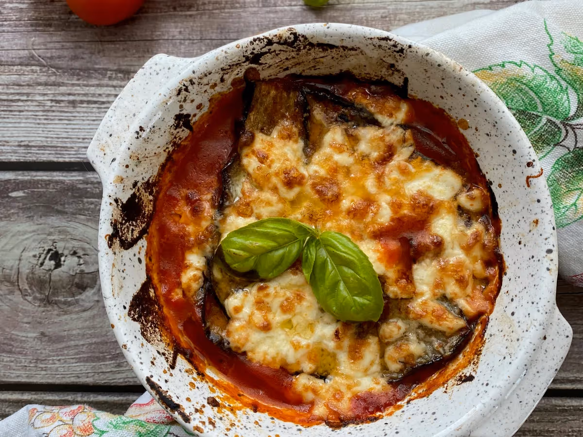 Parmigiana di melanzane in cocotte bianca con mozzarella dorata gratinata e foglie di basilico fresco