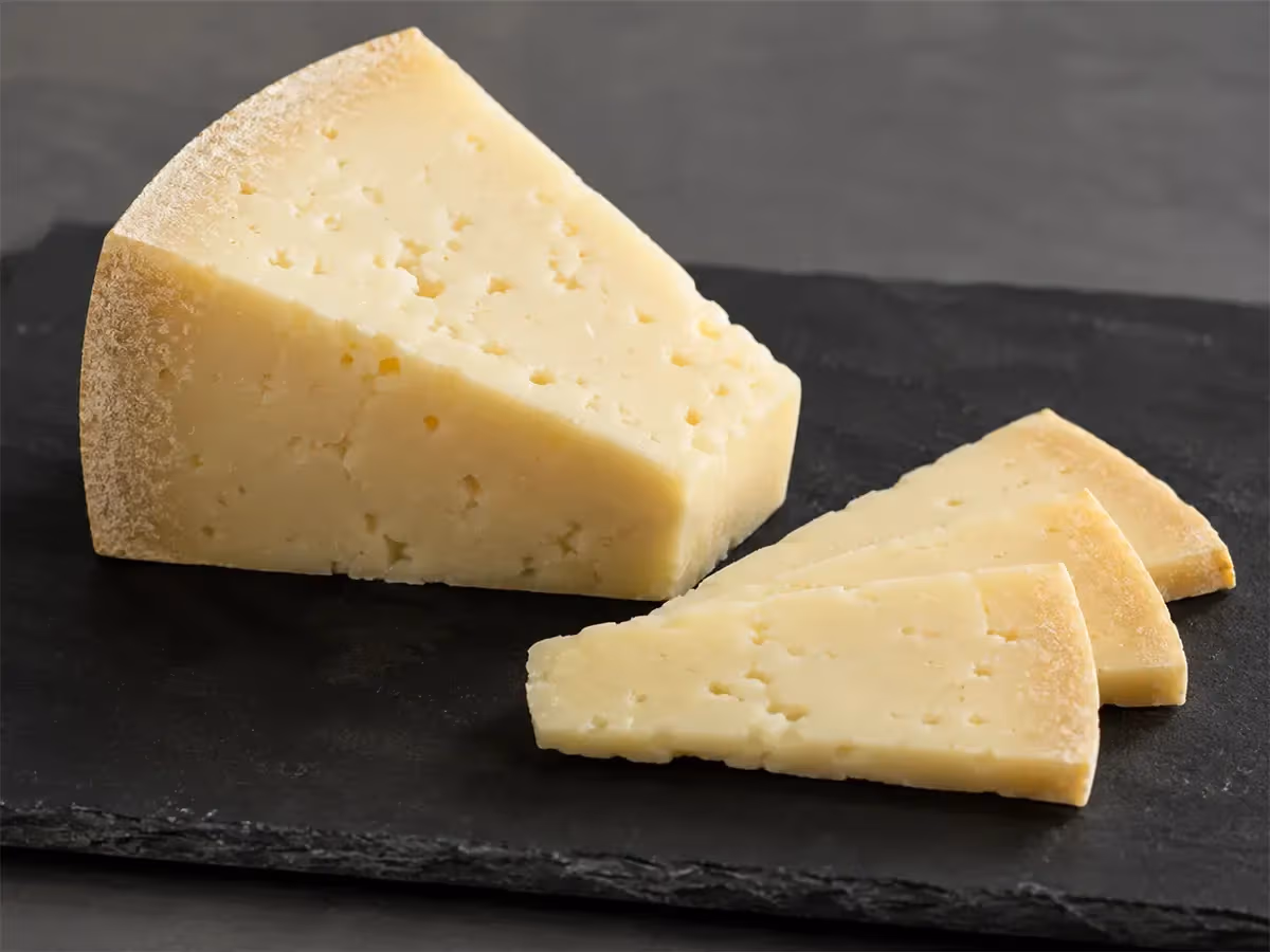 Fetta grande di formaggio stagionato a pasta compatta con tre fettine sottili su ardesia scura