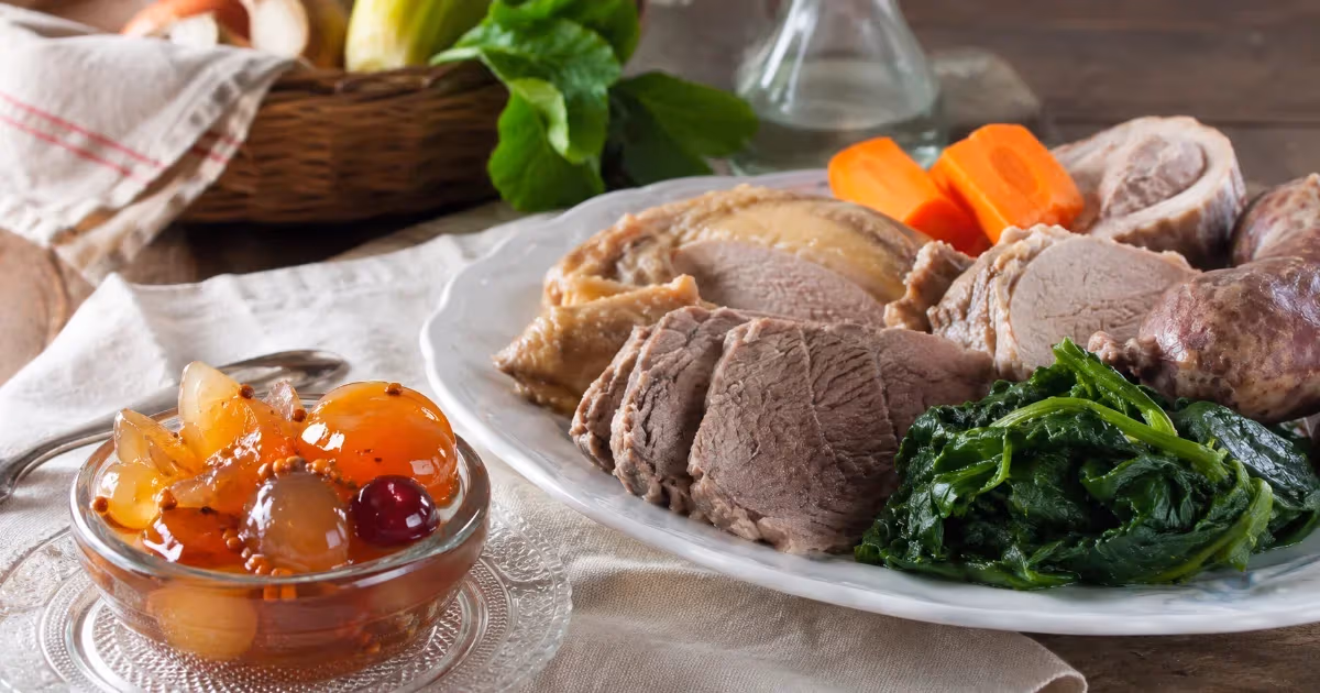 Bollito misto affettato su piatto bianco con spinaci carote e mostarda di frutta in ciotola di vetro