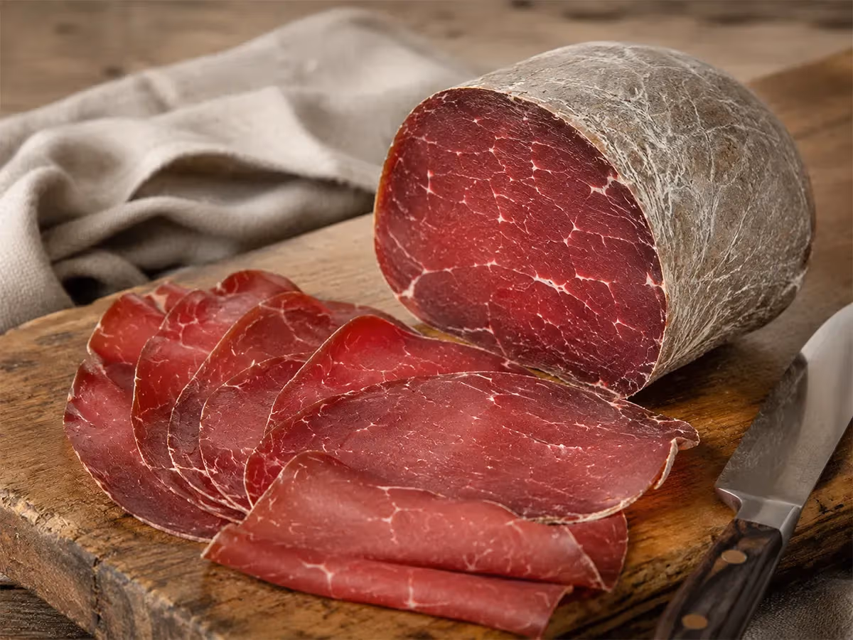 Bresaola della Valtellina IGP affettata su tagliere in legno con crosta grigia e marezzatura visibile