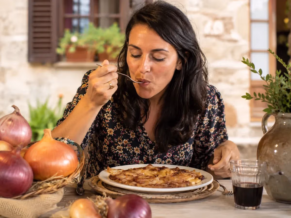 Donna assaggia una torta di cipolle caramellate a tavola con cipolle di Cannara fresche intorno
