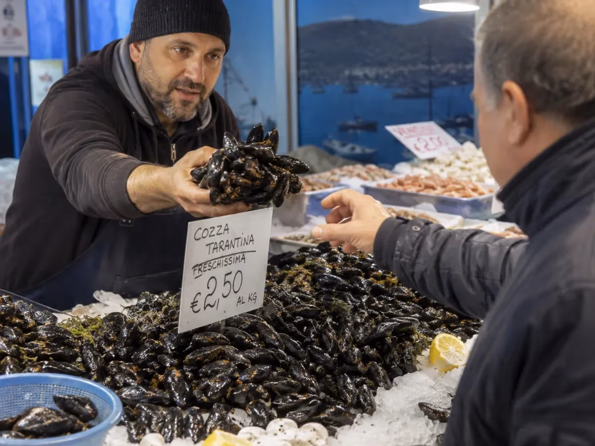 Pescivendolo porge manciata di cozza tarantina fresca al cliente al banco del mercato