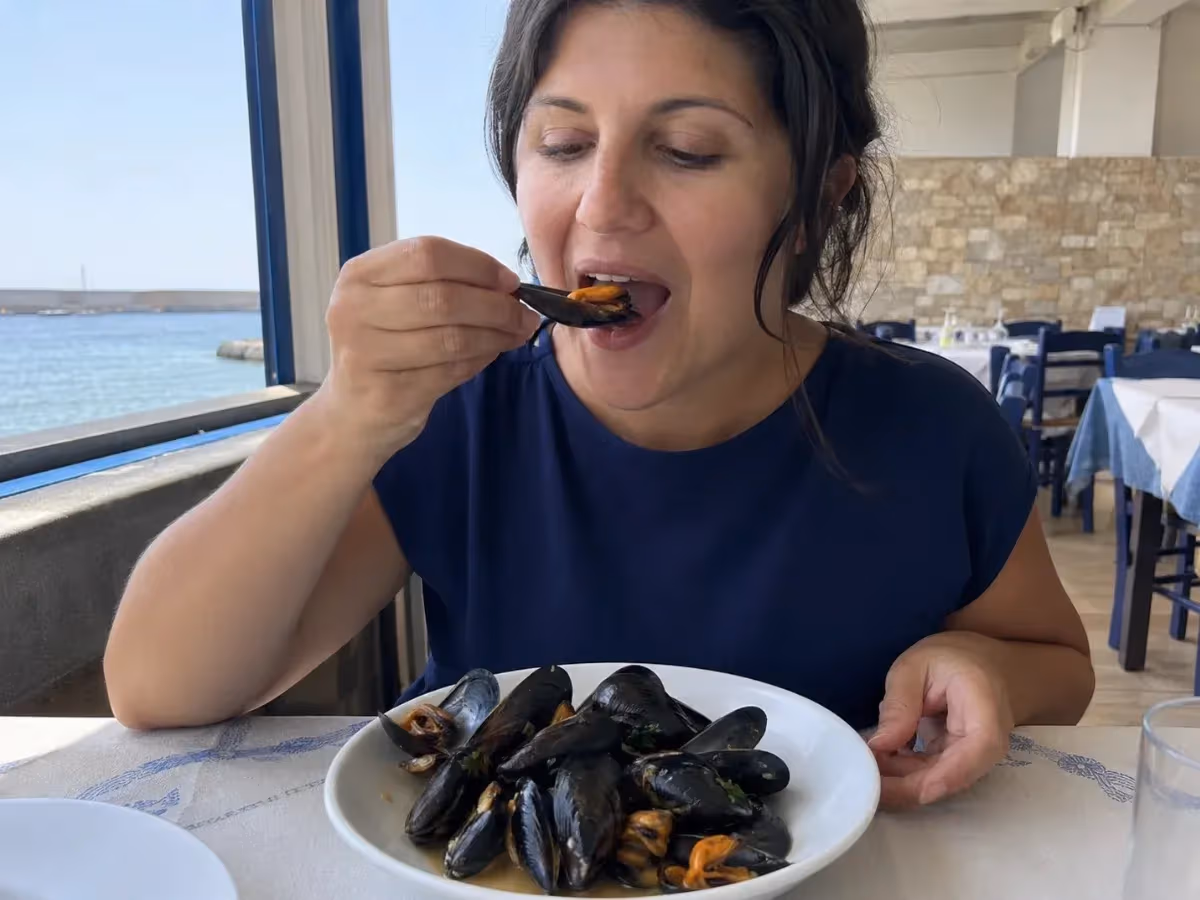 Donna assaggia cozze cotte in piatto bianco in ristorante affacciato sul mare azzurro