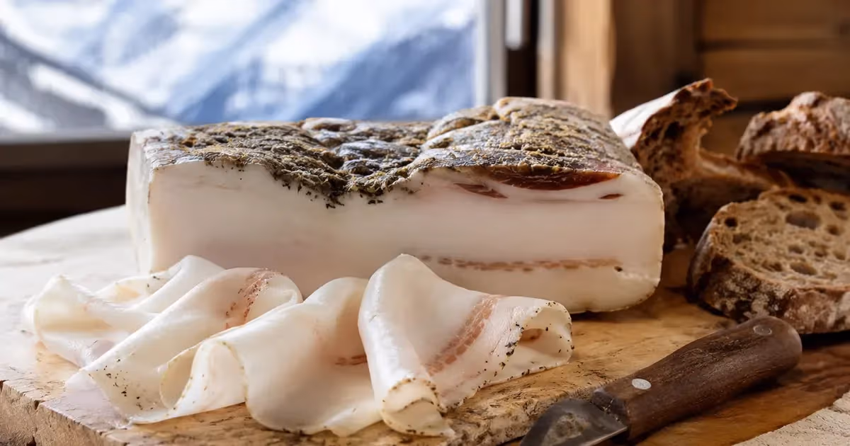 Lardo di Arnad DOP a fette sottili su tagliere rustico con crosta aromatica alle erbe e pane casereccio sullo sfondo montano