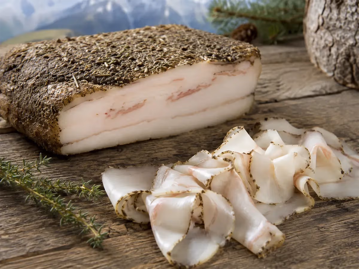 Pezzo intero di lardo di Arnad DOP con crosta scura di spezie e fette bianche con striature rosa su legno