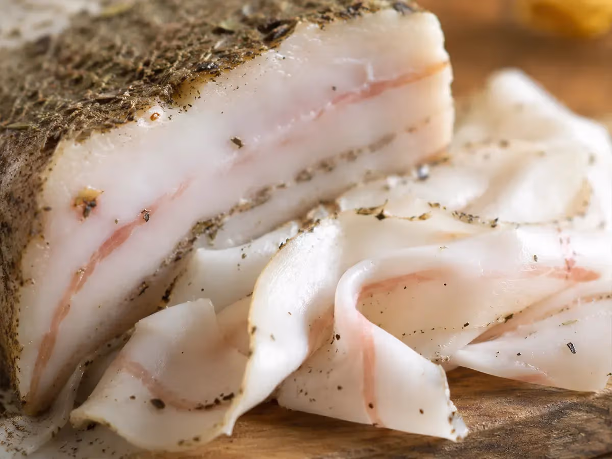 Lardo di Arnad DOP affettato sottile su tagliere con crosta scura di spezie in primo piano