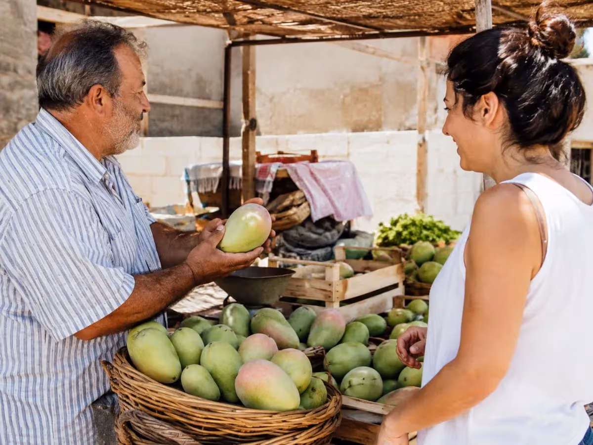 Venditore mostra un mango verde a cliente femminile al banco di mercato rurale all'aperto
