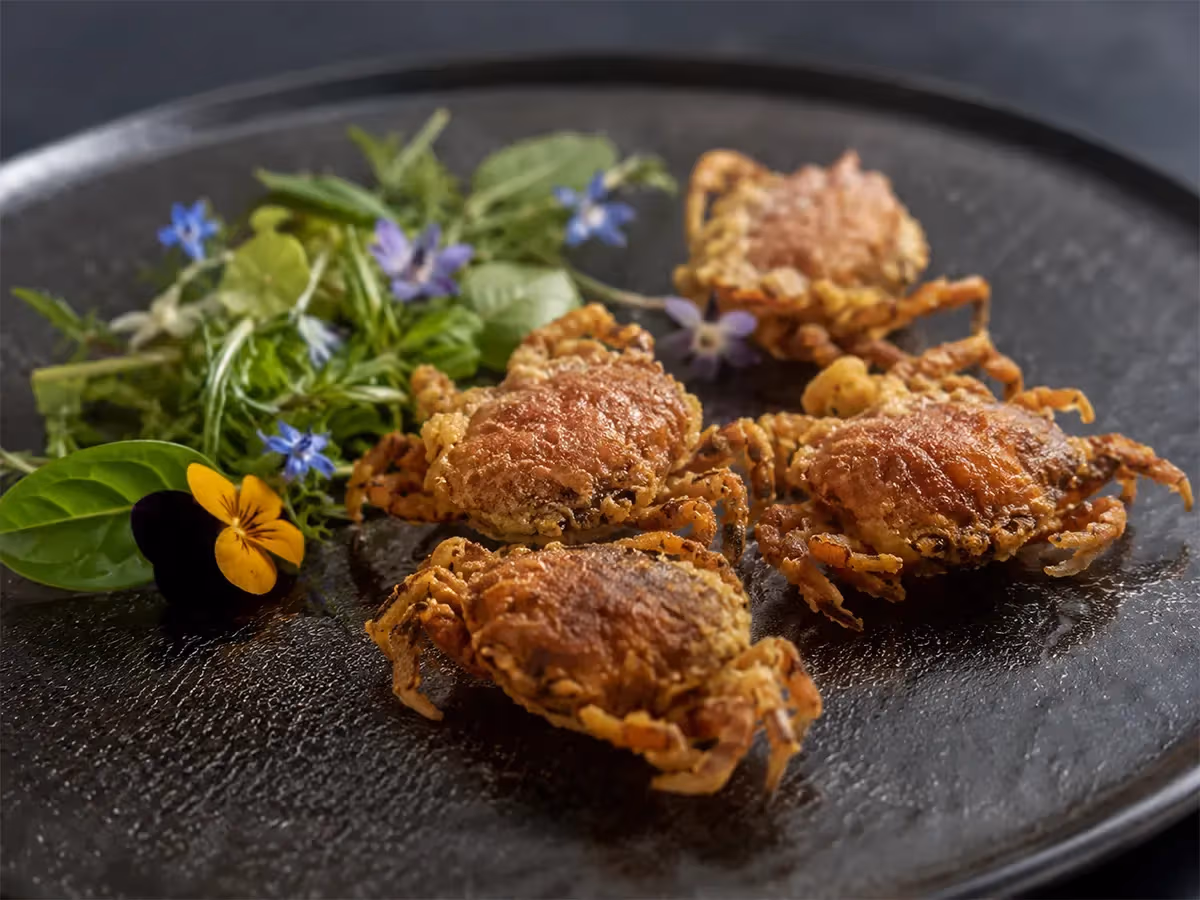 Moeche fritte croccanti su piatto nero con insalatina di erbe e fiori eduli colorati