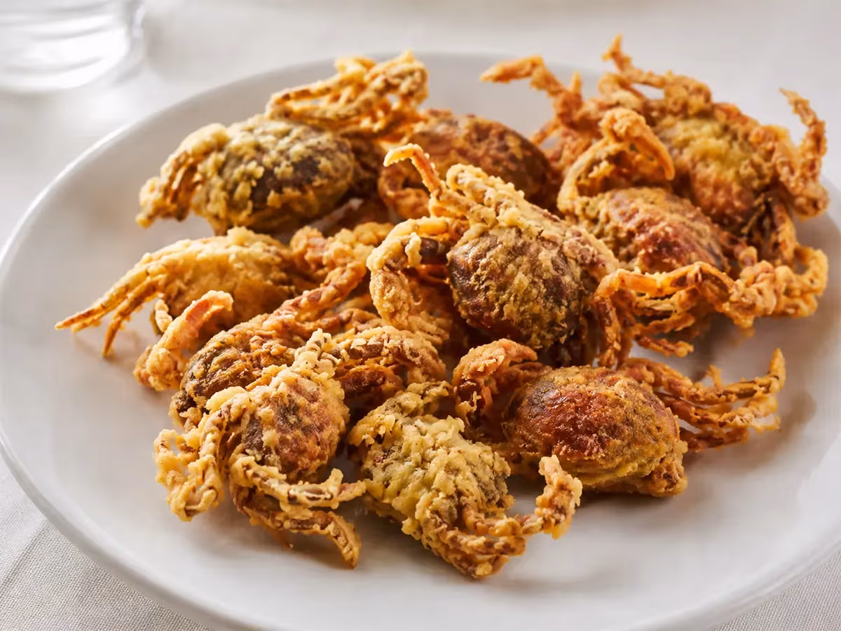 Porzione generosa di moeche fritte con pastella dorata e zampe croccanti su piatto bianco rotondo