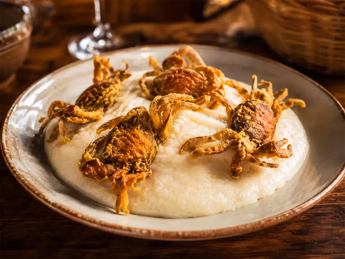 Moeche fritte dorate adagiate su crema bianca cremosa in piatto rustico con bicchiere di vino