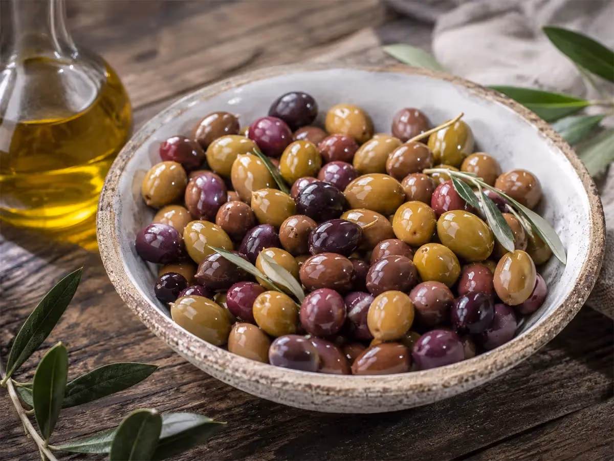 Ampia ciotola rustica di olive miste gialle viola e rosse lucide con ramoscelli e olio extravergine