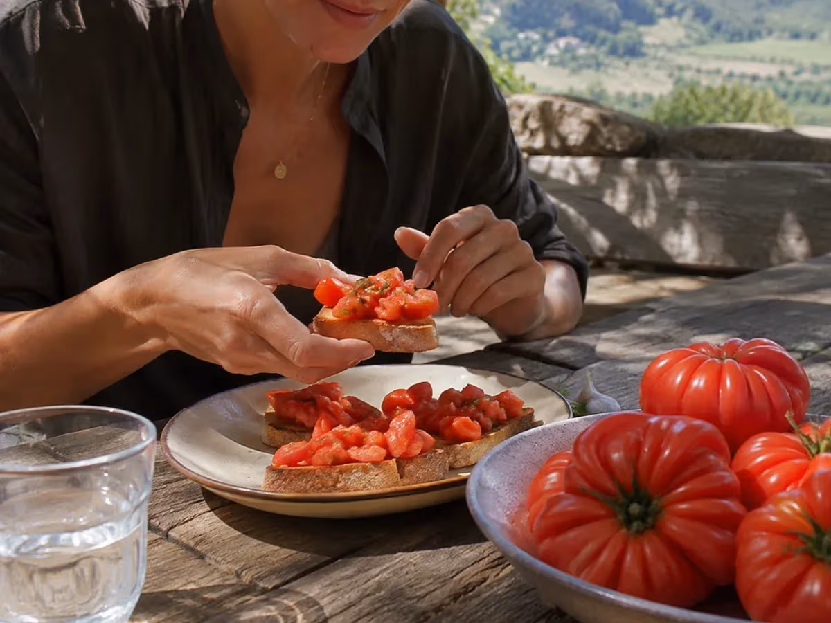 Bruschette con pomodoro costoluto fiorentino a pezzi preparate su tavolo di pietra con vista collinare