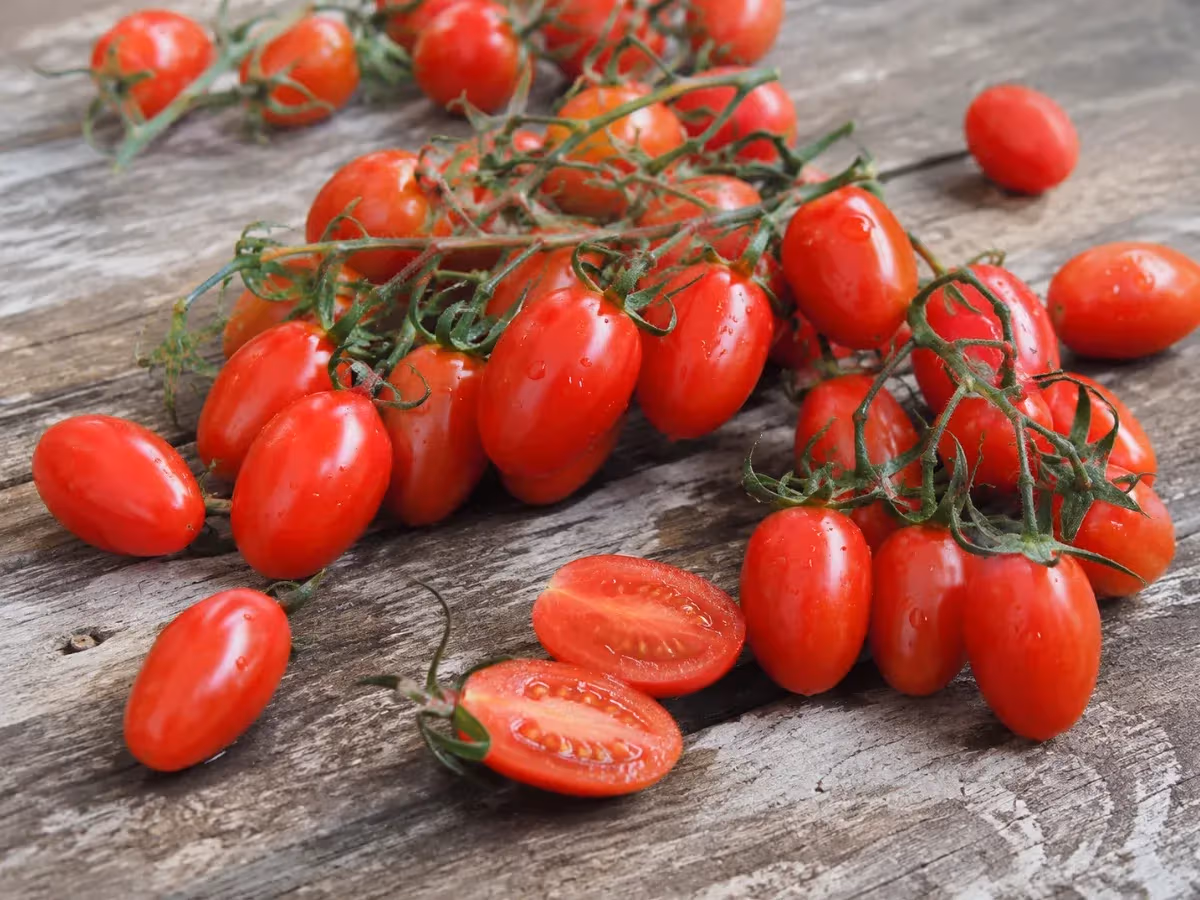 Pomodori datterino rossi lucidi con piccioli verdi su superficie in legno grezzo uno tagliato a metà