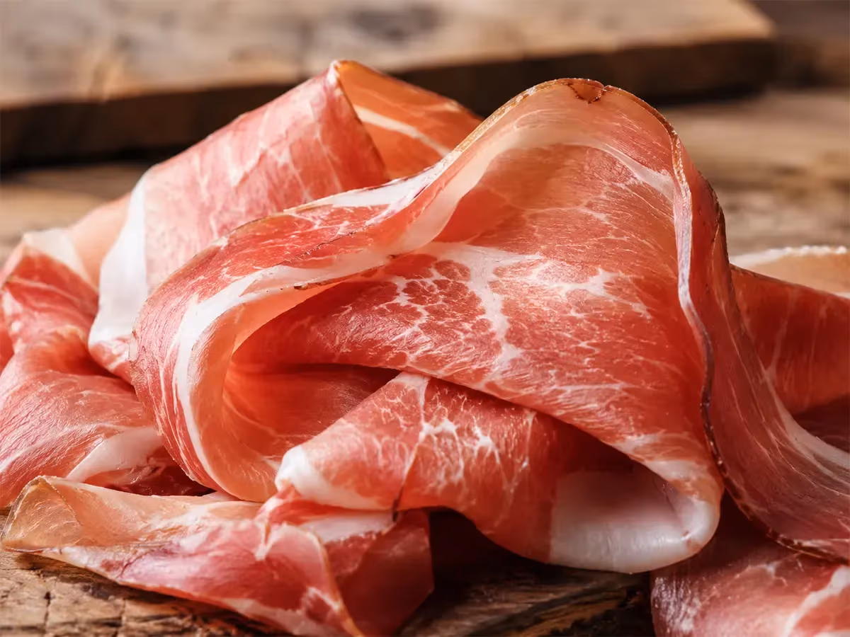 Primo piano di fette di prosciutto crudo arrotolate con venature di grasso bianco su legno