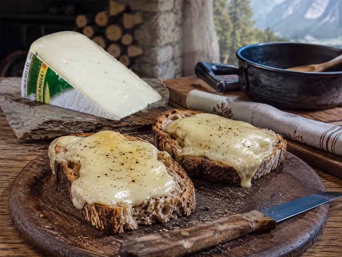 Fette di pane rustico tostate con formaggio Toma filante e pepe nero su tagliere di montagna