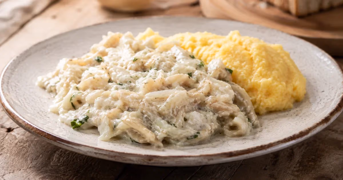 Baccalà alla vicentina cremoso con erbe verdi servito accanto a polenta gialla morbida su piatto rustico